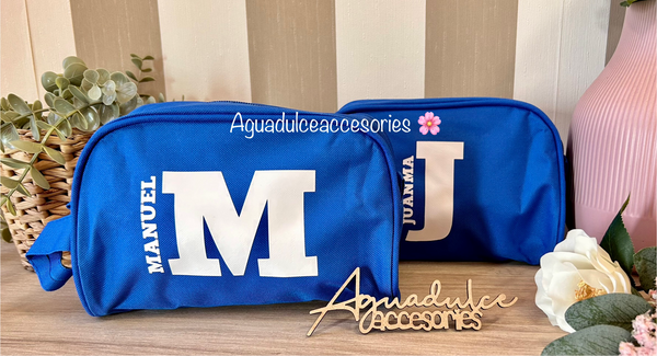 Neceseres azules personalizados con inicial grande y los nombres Manuel y Juanma en blanco.
